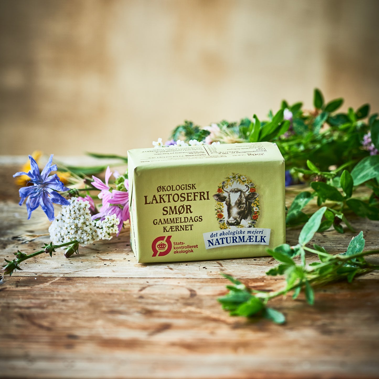 Økologisk laktosefri smør fra Naturmælk omgivet af friske blomster og urter