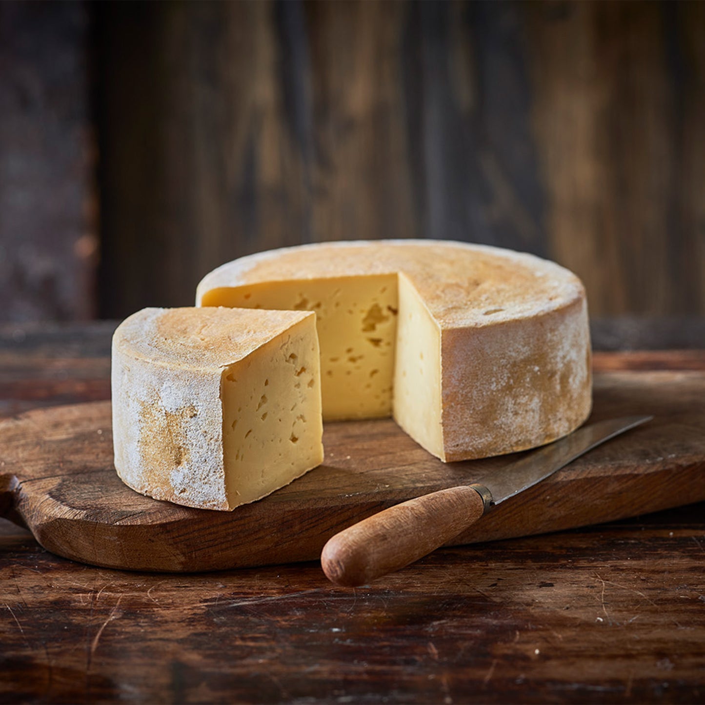 Osteskive på træbræt med kniv og hel ost bagved