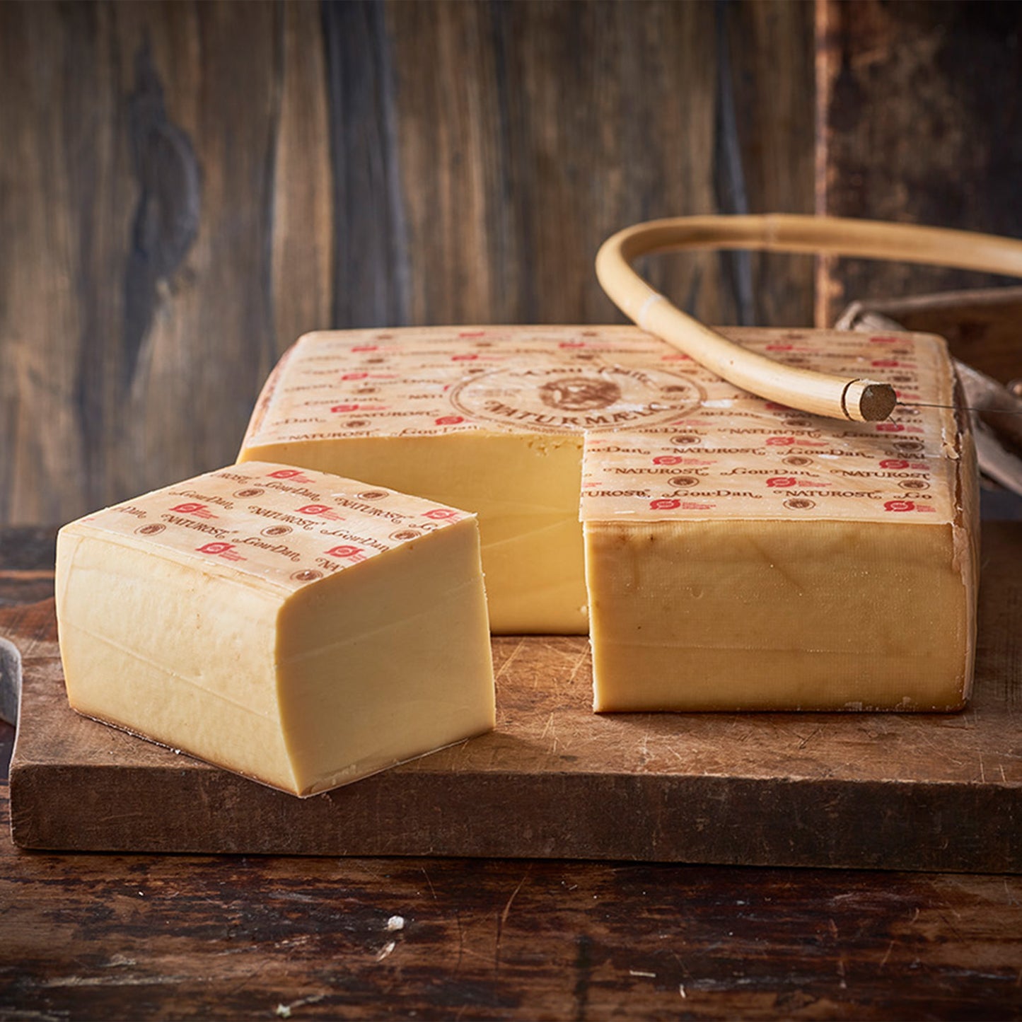 Halvt ostehjul og stykke på træbræt med ostehøvl