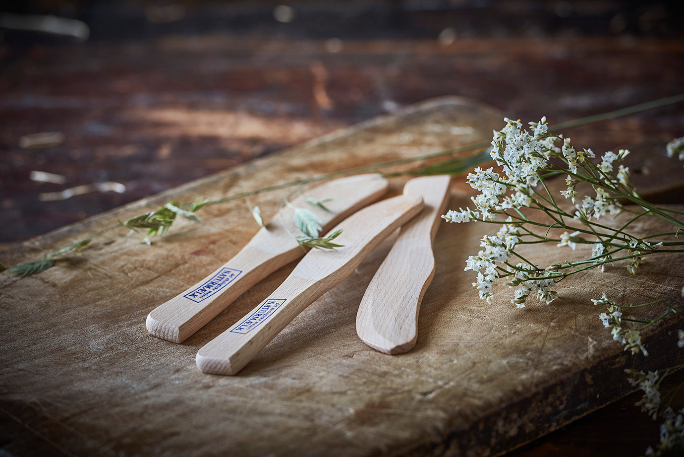 Træsmørknive med Naturmælk logo og hvide blomster på rustikt skærebræt
