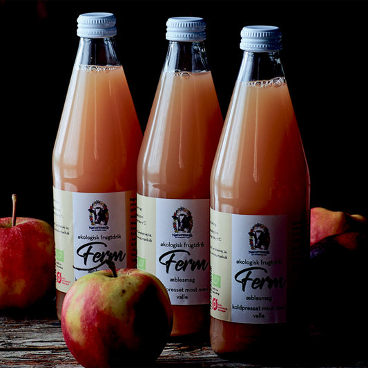 Tre flasker økologisk Ferm frugtdrik med æble fra Naturost.dk omgivet af friske æbler.