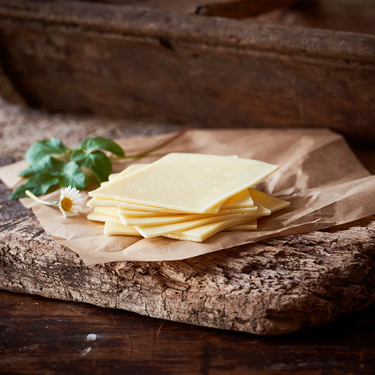 Naturost.dk skiver af ost med frisk blomst på papir og træbord.